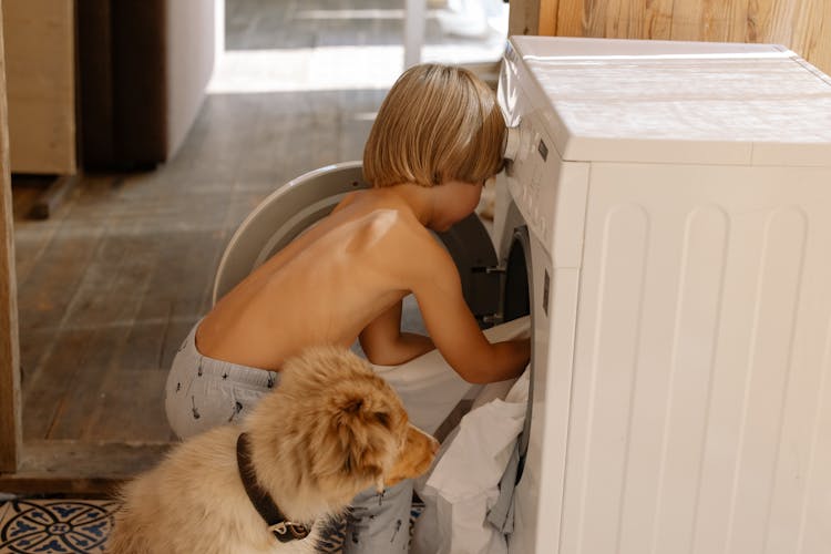 A Young Boy Putting Clothes In Washing Machine