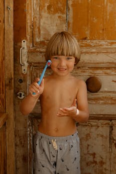 Cute child smiling and holding a toothbrush in a rustic wooden setting, promoting dental care.