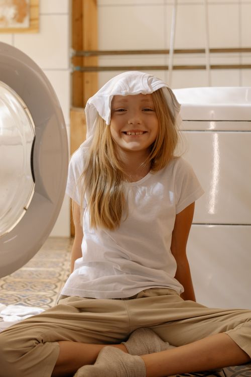 Free Happy blonde girl sitting in laundry room playing with clothes and smiling. Stock Photo