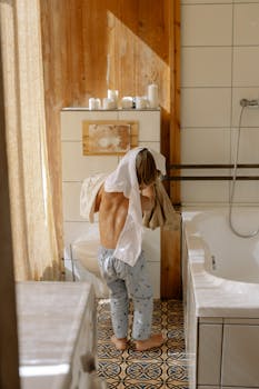A young boy stands in a serene, Scandinavian-style bathroom putting on a shirt.