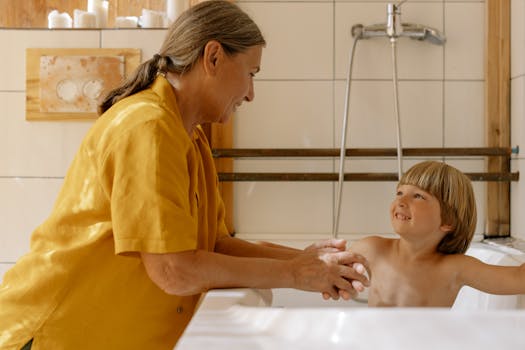 A grandmother helps her happy grandson bathe in an inviting bathroom setting.
