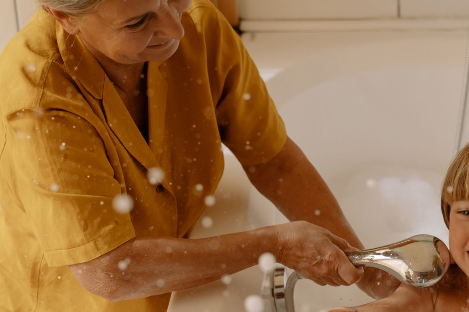 Elderly woman using shower head to bathe her grandson in the bathtub.
