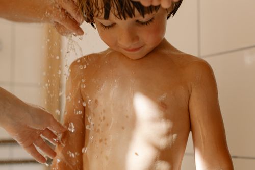 Free A young child receiving a gentle bath assistance with sunlight filtering through. Stock Photo