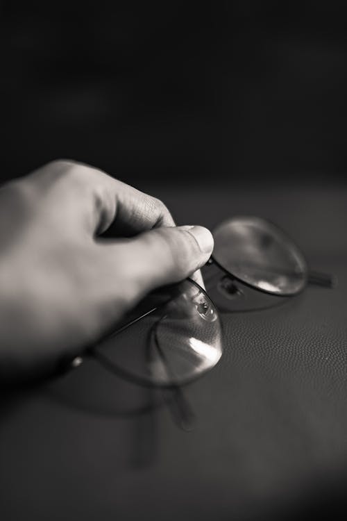Black and white hand of crop unrecognizable person with stylish eyeglasses for vision on table sitting in room at home