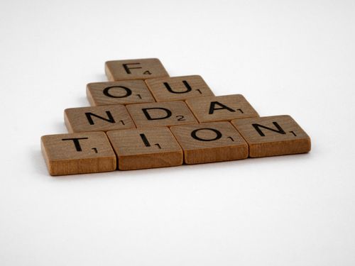 Free Scrabble tiles arranged to spell 'Foundation' on a white surface. Stock Photo