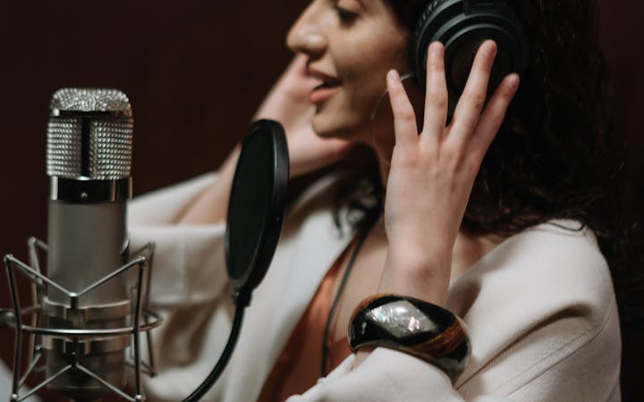 Woman singing in a music studio while recording vocals with headphones and microphone.