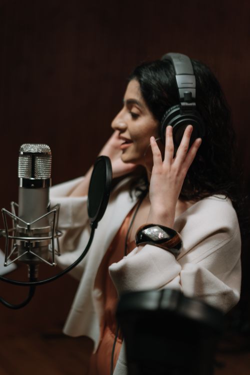Free Woman singing in a music studio while recording vocals with headphones and microphone. Stock Photo