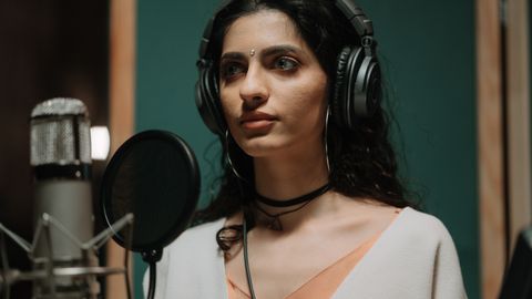 Female singer recording vocals in a professional music studio wearing headphones.