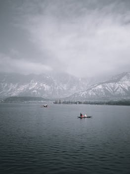 Tranquil boat scene on a mountainside lake with snowy peaks and cloudy skies.