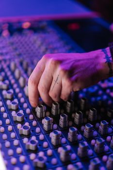 Close-up of a hand with tattoo adjusting knobs on a professional audio mixing console in a music studio.