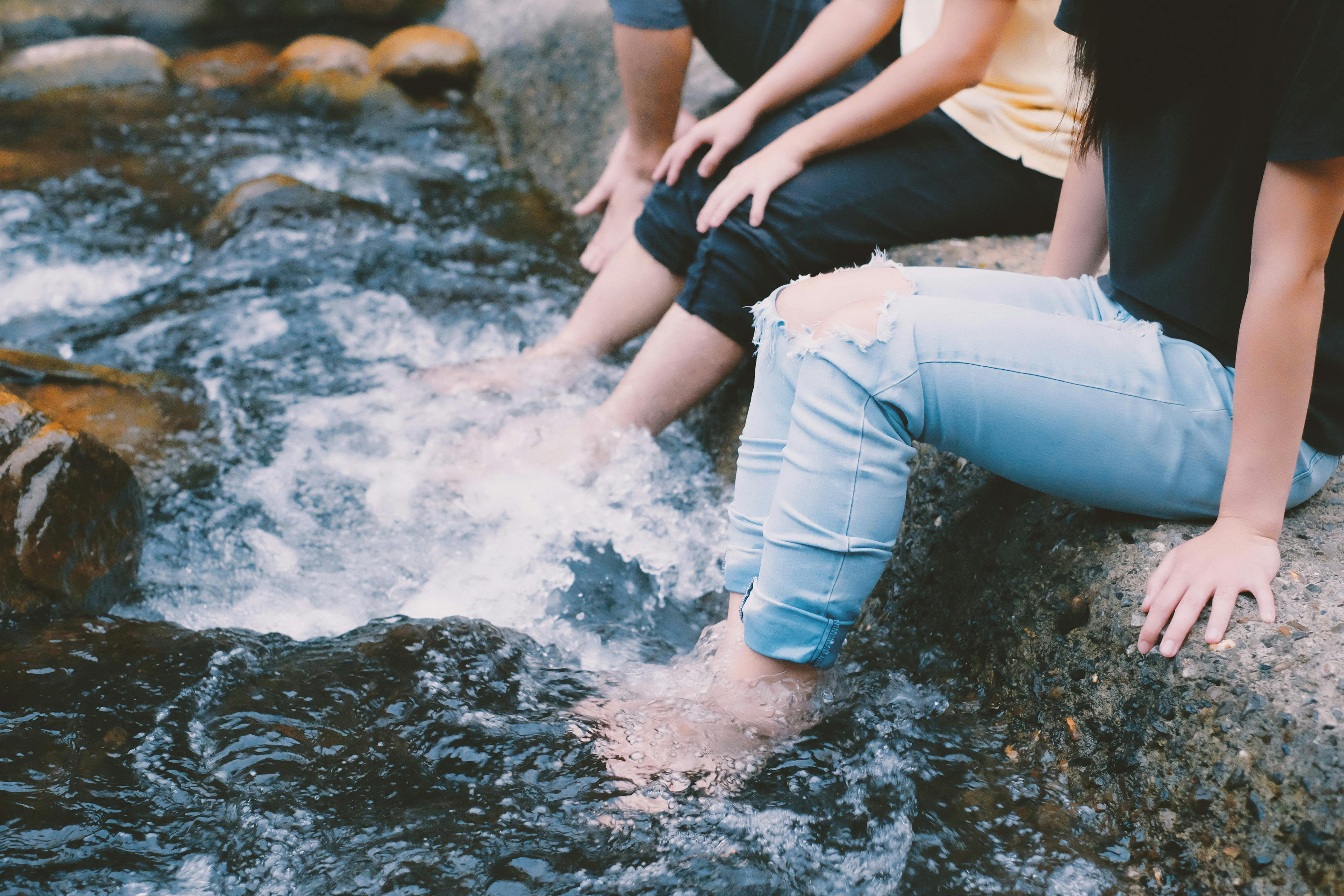 Two people enjoying leisure time by a rocky stream, feeling the cool water.