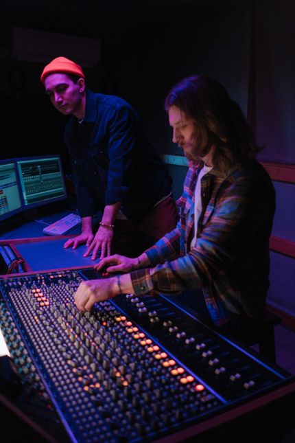 Two engineers working a console in a dim control room — photo by cottonbro studio on Pexels