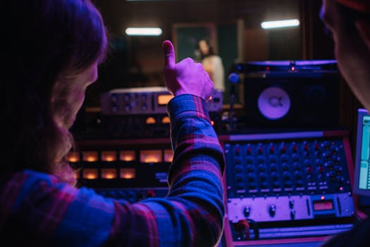 Audio engineer gesturing thumbs up in a vibrant music studio with equipment.