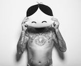 A Shirtless Man with Tattoo on His Body Covering His Face with Stuff Toy