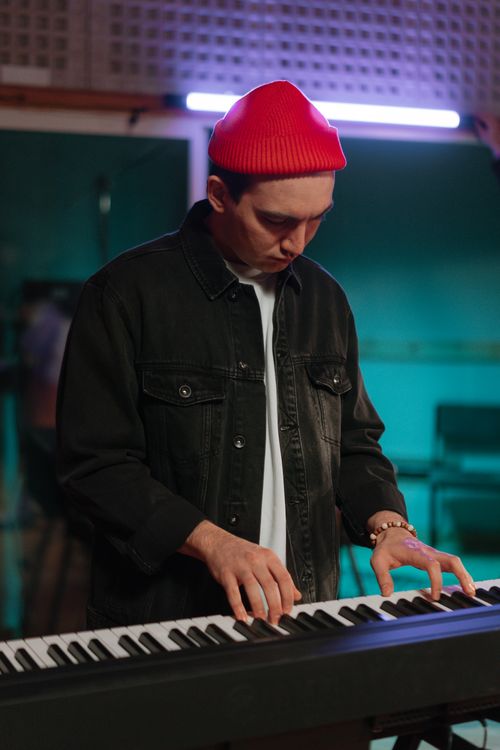 Free A man wearing a red beanie plays the keyboard in a music studio setting. Stock Photo