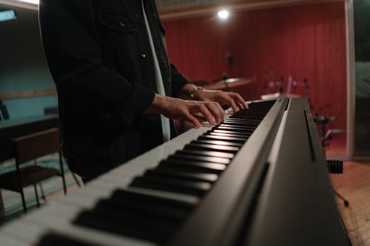 Musician playing a keyboard in a studio setting, focusing on hands and instrument.