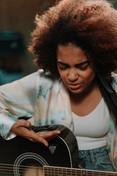 Black woman passionately playing an acoustic guitar in a music studio.