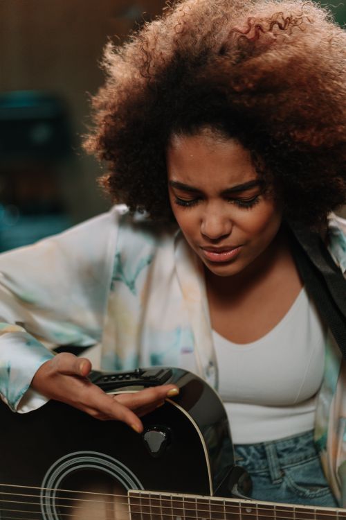 Free Black woman passionately playing an acoustic guitar in a music studio. Stock Photo