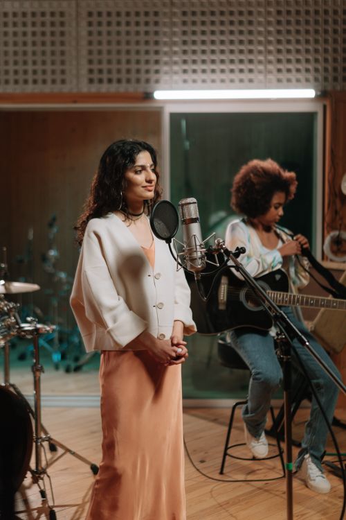 Free A female vocalist records vocals in a music studio while a guitarist accompanies her, capturing a dynamic musical scene. Stock Photo