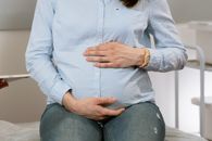 Pregnant woman sitting indoors, hands on belly, wearing casual clothes. Healthcare consultation setting.