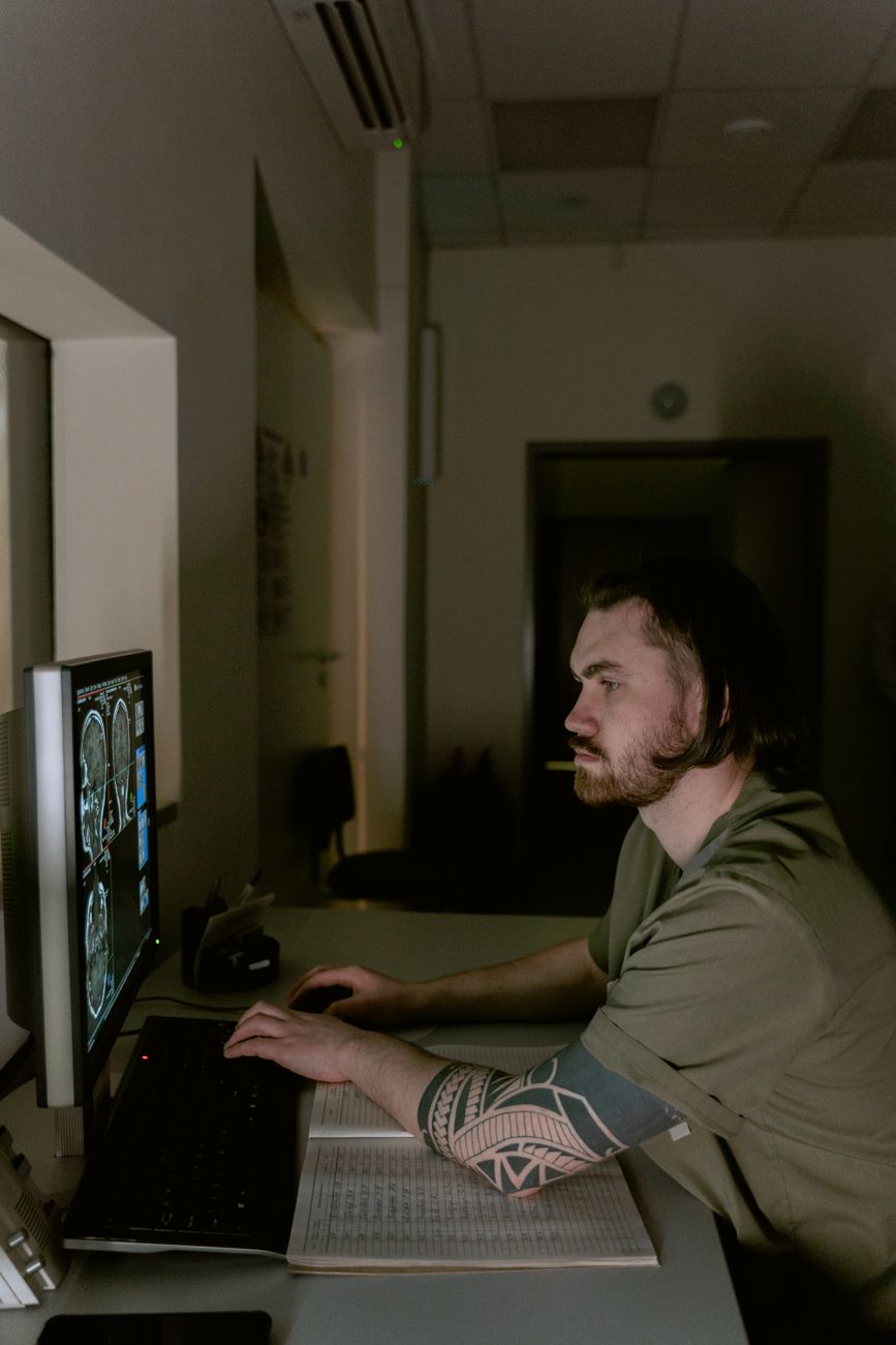 Radioloog onderzoekt hersen-CT-scans op een computermonitor in een slecht verlichte medische kantoor.