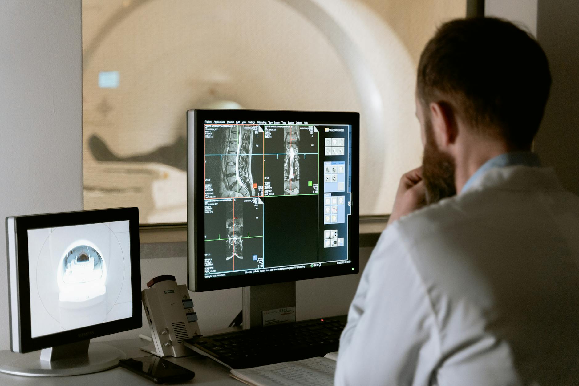A radiology technician looks at the monitor while the patient in the adjoining room receives a computed tomography (CT) scan.