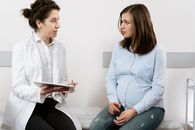 A pregnant woman consulting with a female doctor in a medical clinic setting.