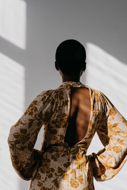 Anonymous graceful black lady in fashionable dress standing near white wall