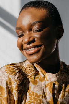 Portrait of a smiling black woman with short hair wearing a floral top, illuminated by natural light.