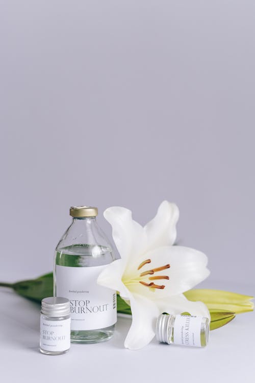 Close-Up Shot of a Bottle of Liquid beside a White Flower