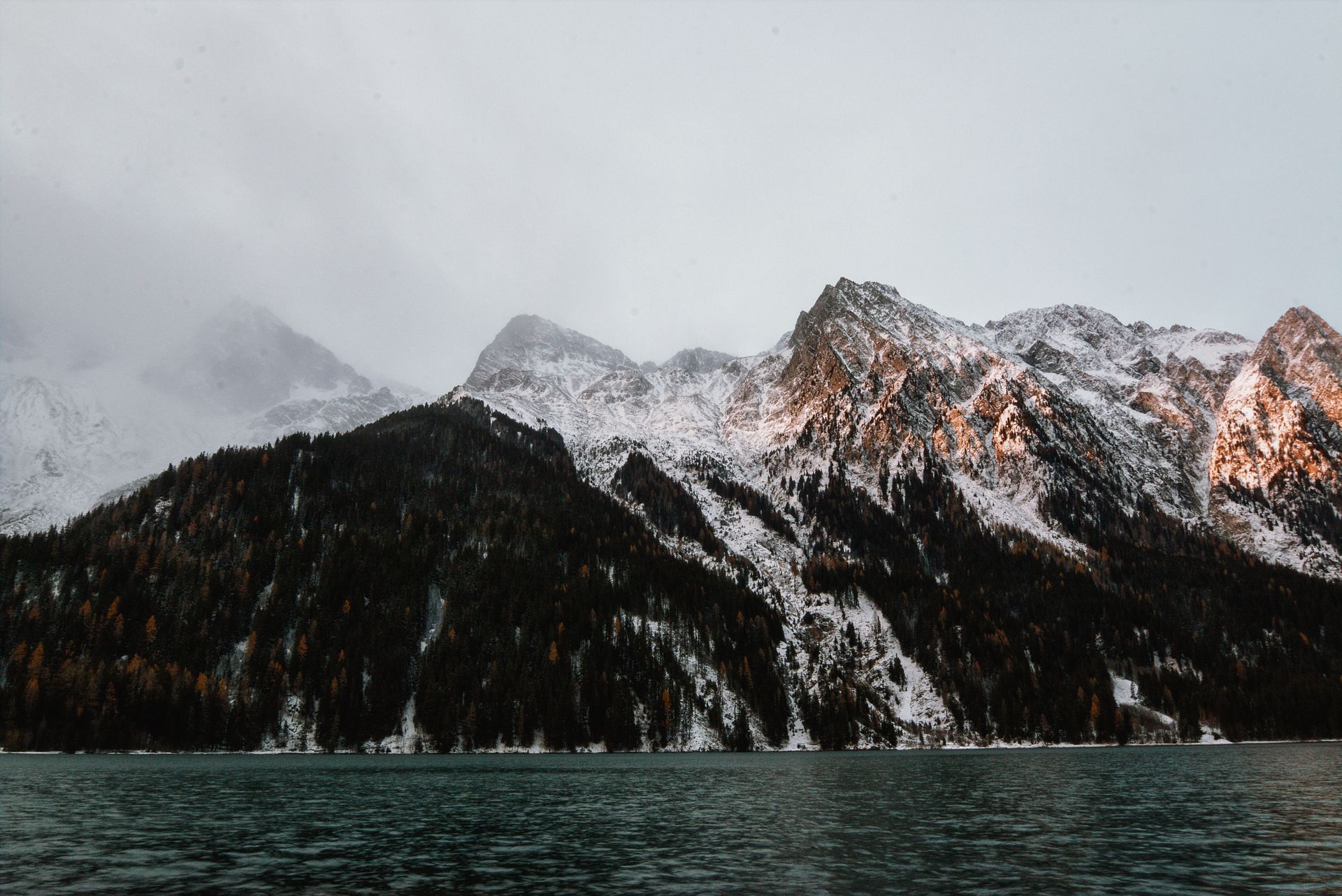 Breathtaking view of a snow-capped mountain range reflected in a serene lake, captured in winter.