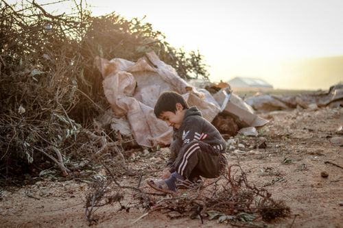Free A boy sitting alone outdoors amidst debris at a dump site in Idlib, Syria. Stock Photo