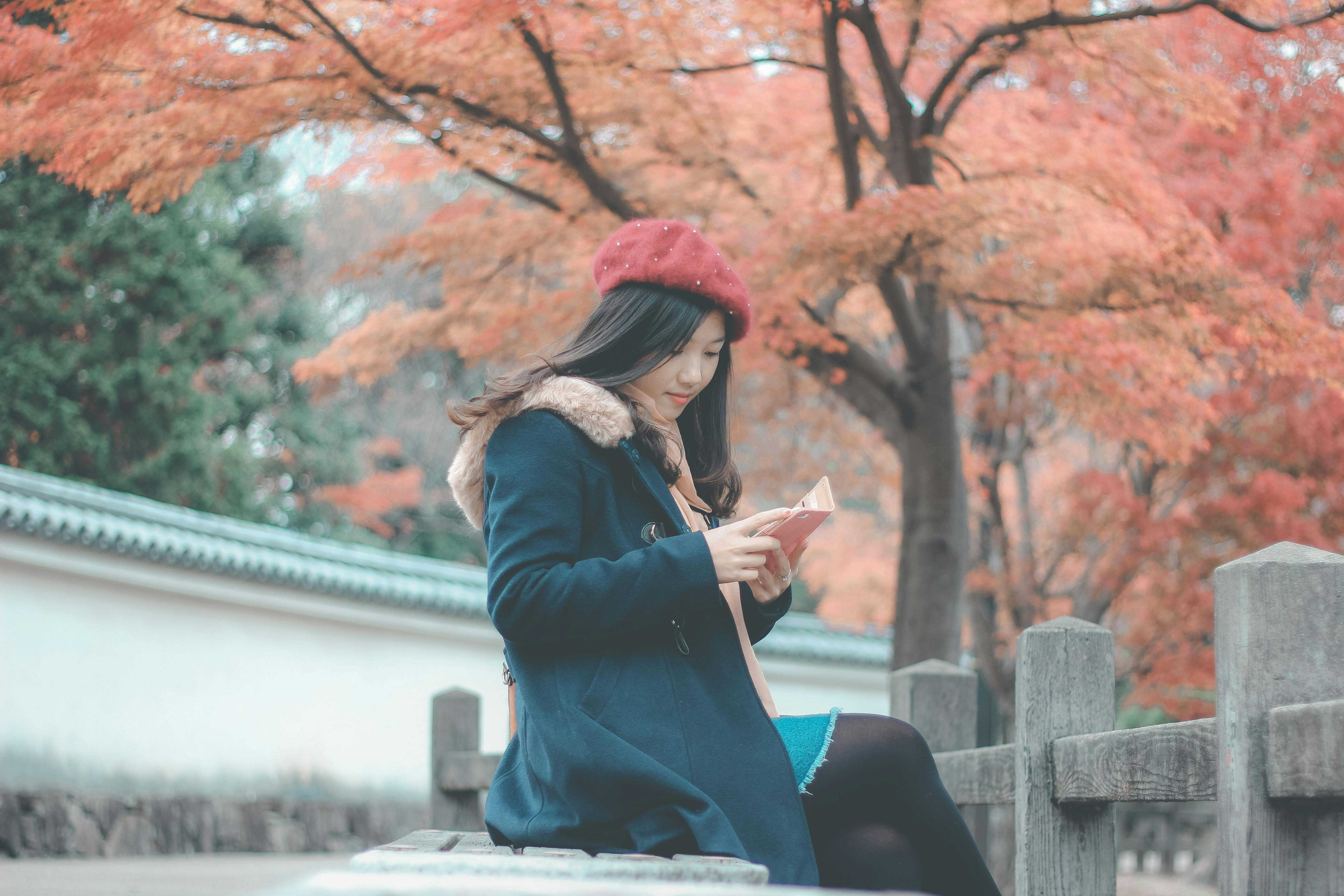 Woman In Blue Parka Jacket Sitting On Grey Concrete Bench Reading
