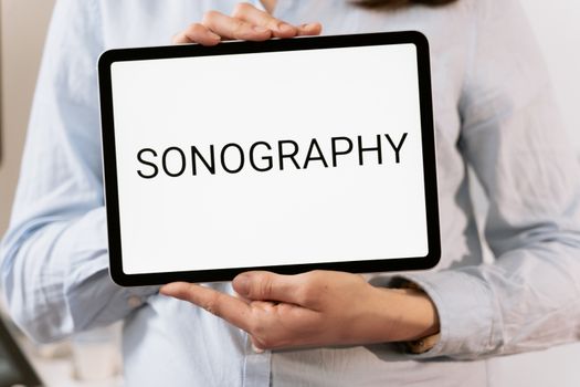 Digital tablet displaying word 'Sonography' held by person in medical setting.