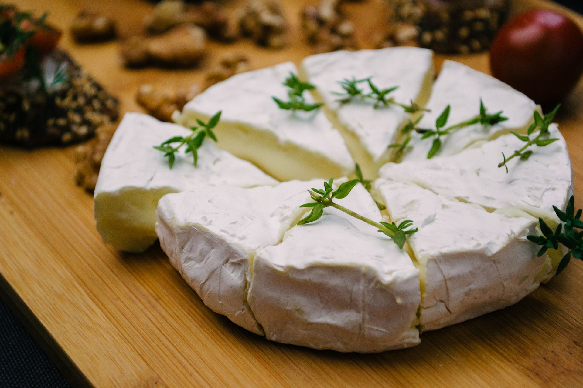 Sliced Brie cheese garnished with herbs on a wooden board, close-up view.