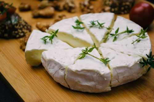 Free Sliced Brie cheese garnished with herbs on a wooden board, close-up view. Stock Photo