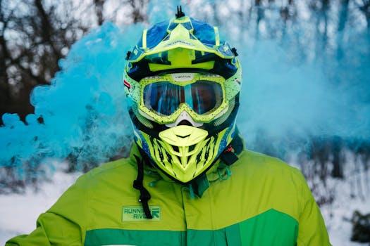 Person wearing vibrant helmet and winter jacket surrounded by blue smoke in a snowy forest setting.