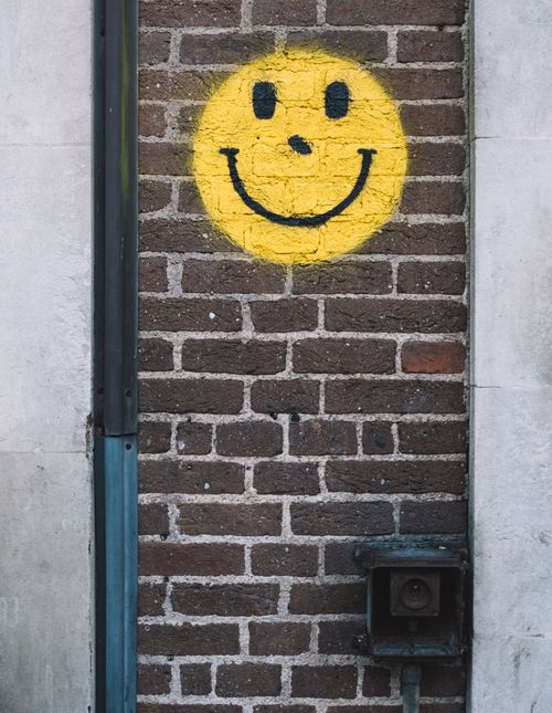 Free Street art smiley face graffiti on urban brick wall with vibrant yellow color. Stock Photo