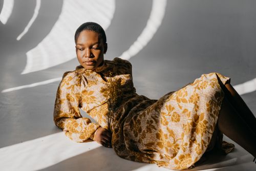 Free Stylish woman in yellow floral dress posing leisurely in artistic shadow lighting. Stock Photo