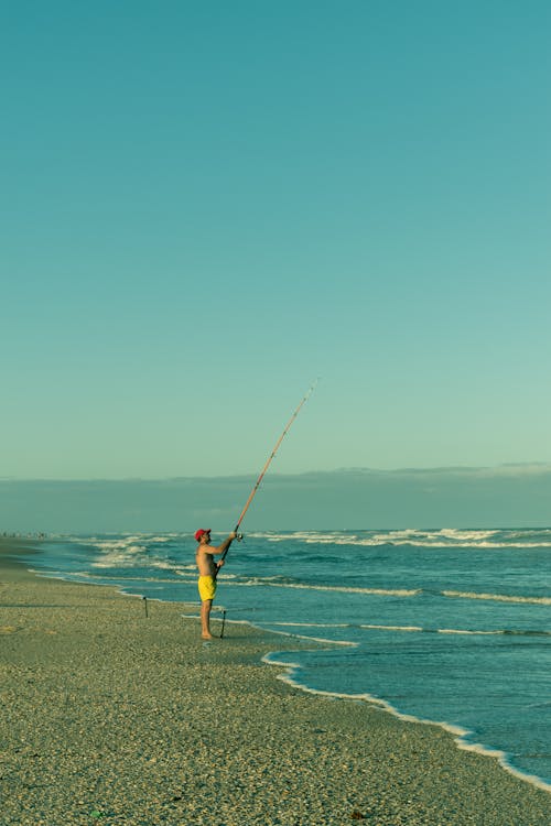 A Shirtless Man Standing on the Beach while Holding a Fishing Rod