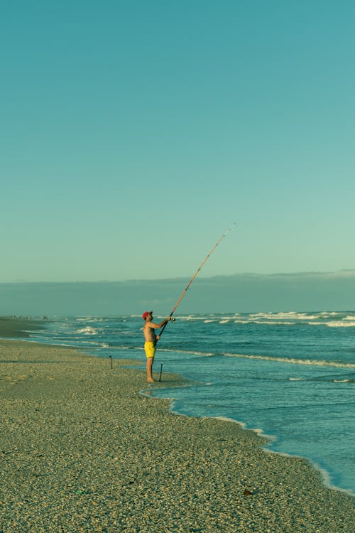 A Man Standing on the Beach while Holding a Fishing Rod