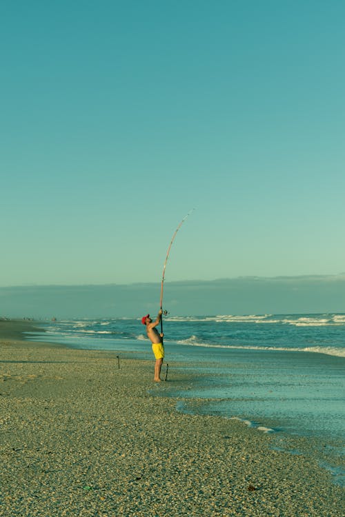 A Shirtless Man Holding a Fishing Rod while Standing on the Beach