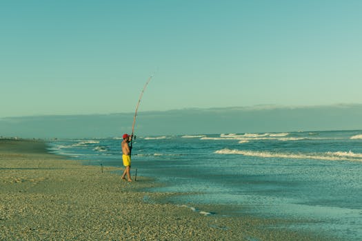 A man enjoys fishing by the ocean on a sunny beach, capturing a peaceful moment.