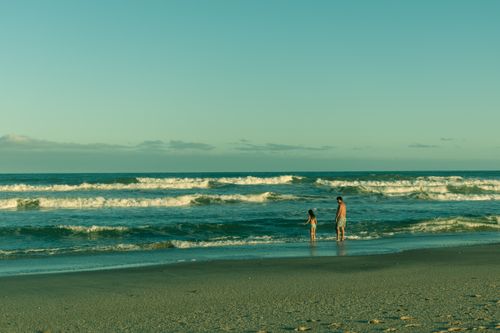 Free A father and daughter enjoy a sunny day at the beach, standing by the ocean waves. Stock Photo