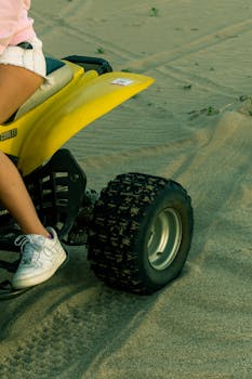 A young adult riding an ATV on a sandy terrain, partial view with focus on wheel and sneaker.