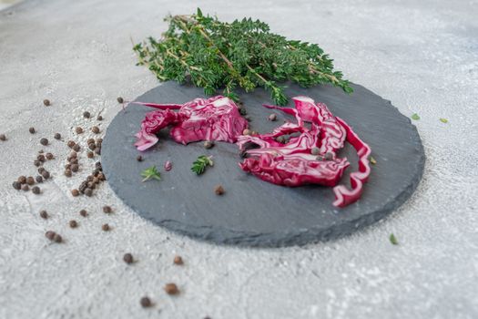 Close-up of sliced red cabbage on slate with fresh herbs and scattered peppercorns.