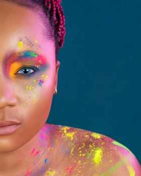 Crop African American woman with colorful paints on face and body and braids looking at camera against blue background