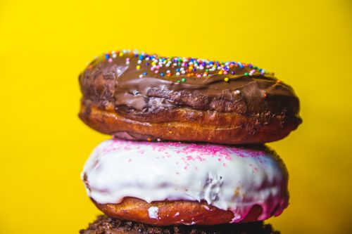 Free Close-up of stacked chocolate and vanilla donuts with sprinkles on a vibrant yellow background. Stock Photo