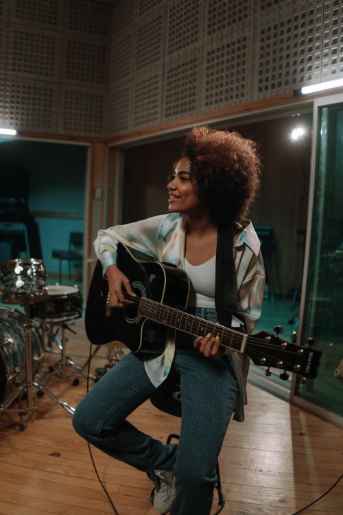 Free Black woman with afro hair playing acoustic guitar in recording studio. Stock Photo
