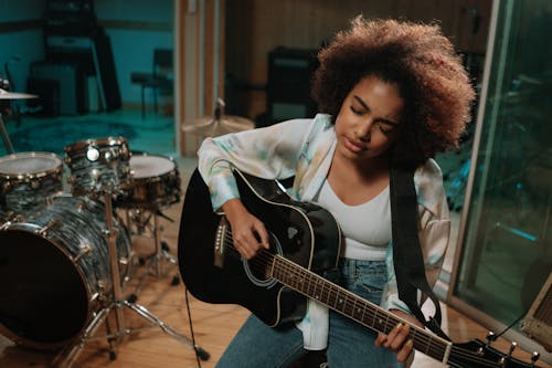 
Afro-Haired Woman Playing Acoustic Guitar in a Recording Studio